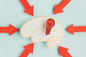 Cérebro com setas apontadas e uma lâmpada no interior, representando gatilhos mentais para vendas.